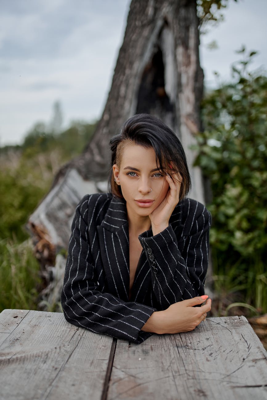 stylish focused woman leaned on hand at table in countryside
